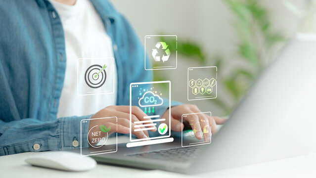 Close-up of person using laptop with net zero and carbon reduction icons, including CO2 cloud, recycling, green energy, and sustainability targets, symbolizing eco-friendly digital innovation.