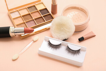 Makeup products with fake lashes on beige background