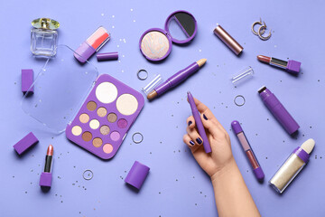Female hand with different decorative cosmetics, perfume and jewelry on purple background