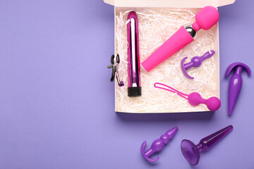 Gift box with different modern sex toys on purple background