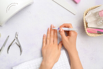 Female hands applying cuticle oil onto fingernails, manicure instruments and towel on light...