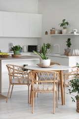 Stylish interior of modern kitchen with armchairs, dining table, houseplants and counters