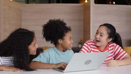 Multicultural girl students feel excited and happy together, sitting at a table and learning with a laptop.