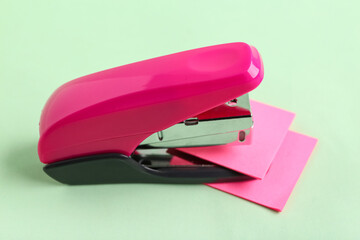 Pink stapler with sticky notes on green background