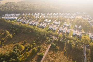 Aerial view of a modern residential development with white houses next to a forest at sunrise