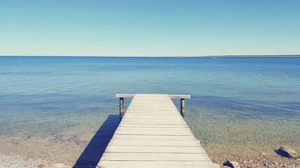Fototapeta premium Serene wooden dock extends into calm, clear turquoise water under a brilliant blue sky. Tranquil beach scene evokes peace and relaxation