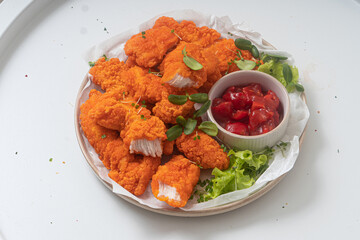 Breaded chicken nuggets with sauce and salad on a plate on a white background