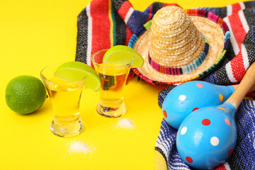 Shots of tequila, lime and maracas on yellow background