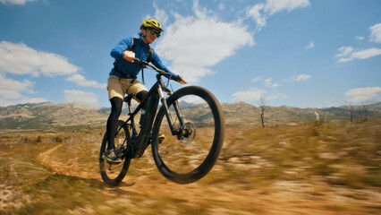 A thrilling mountain biking adventure unfolds as a man, donned in a blue shirt and yellow helmet, skillfully navigates a dirt trail. The dynamic perspective captures the bike's front wheel mid-air.