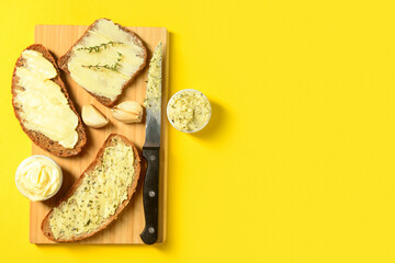 Wooden board of bread slices with fresh butter and garlic on yellow background