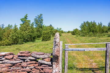 Gate to a dirt road with a limestone slate stone wall on a meadow