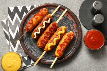 Plate with tasty corn dogs and bowls of different sauces on grey background