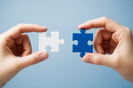 Two hands holding matching puzzle pieces symbolizing connection and teamwork on a light blue abstract background, perfect business concept image.