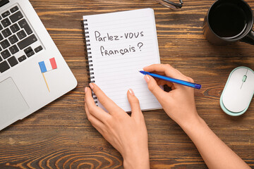 Woman writing in French, modern laptop and cup of coffee on wooden table, closeup