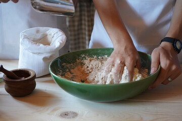 A child’s hands mixing water with flour to make dough in a green ceramic bowl during a...