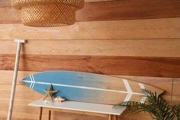 Shelf with surfboard, houseplant and paddle near wooden wall in room
