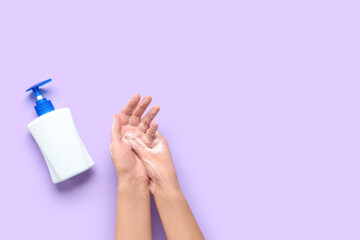 Woman with bottle of sanitizer washing hands on purple background