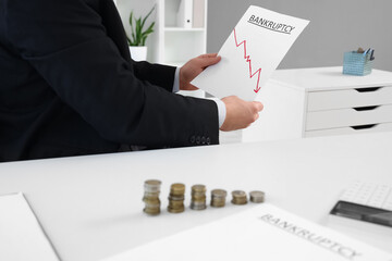 Young businessman holding paper with word BANKRUPTCY in office, closeup