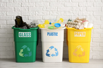 Full trash bins with different types of garbage near white brick wall. Recycling concept