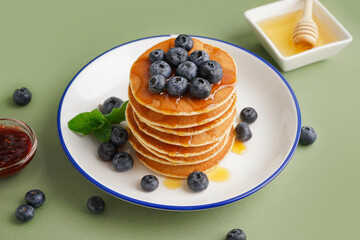 Plate with tasty pancakes and bowl of honey on green background