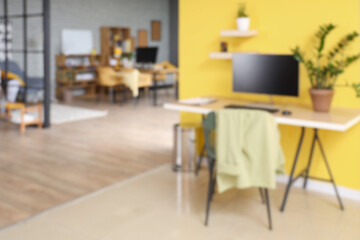 Blurred view of stylish office with desks, plants and yellow wall
