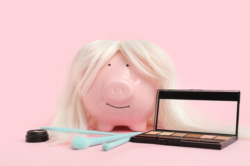 Piggy bank in wig with makeup supplies on pink background