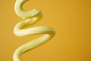 A circular swirl of pale yellow cream creates an elegant spiral pattern against a solid golden yellow background. The cream forms a continuous flowing line that starts from the outer edge and coils in