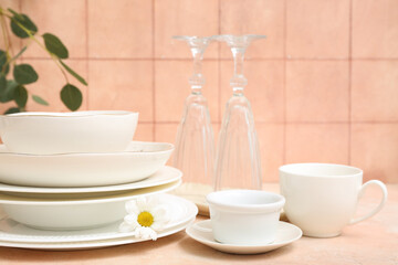 Beautiful tableware and chamomile on table near orange tile wall