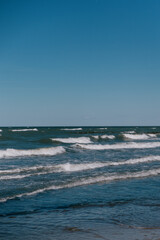  ocean is calm, the sky is clear. The water is blue and the waves are small. The sky is clear and blue. a tourist destination, a marine area with a sandy beach for walking.