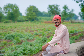 young indian farmer standing at green agricultural field