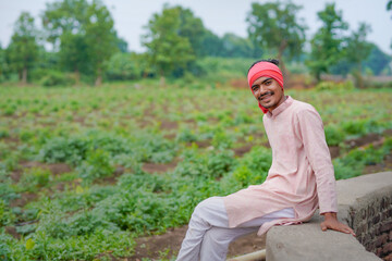 young indian farmer standing at green agricultural field