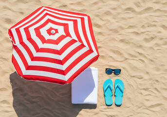 A top-down view of summer beach essentials, including a striped umbrella, towel, sunglasses, and flip-flops on the sand, with copy space.