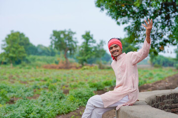young indian farmer standing at green agricultural field