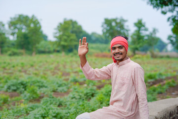 young indian farmer standing at green agricultural field