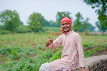 young indian farmer standing at green agricultural field