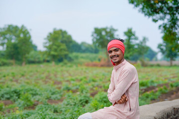 young indian farmer standing at green agricultural field