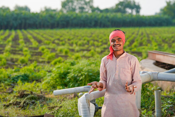 young indian farmer standing at green agricultural field