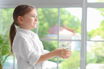 Cute little girl with glass of water near window at home