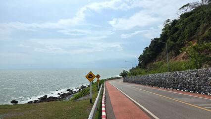 Scenic coastal road with curve signs beside Khung Wiman Beach, Chanthaburi, Thailand, showing sea,...