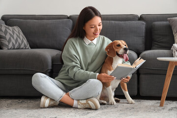 Young woman reading book and sitting with cute Beagle dog on floor in living room
