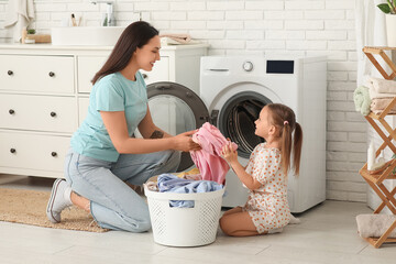 Young woman and her little daughter doing laundry at home