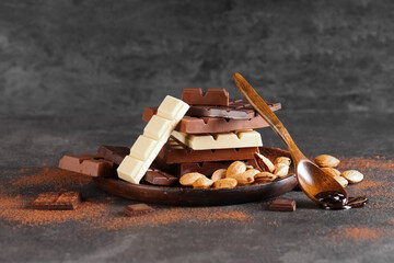 Plate with different sweet chocolate bars and almond nuts on dark background