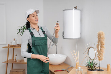 Female worker with flexible hoses near modern electric boiler in bathroom