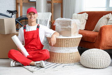 Male worker with roll of stretch film sitting on floor in room