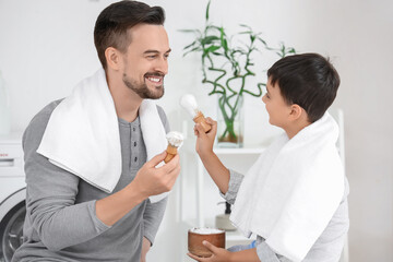 Happy father and his little son with brushes applying shaving foam on their faces in bathroom