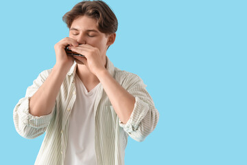 Young man playing harmonica on blue background