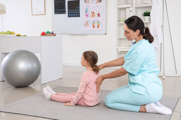 Female osteopath with little patient stretching and doing exercises in clinic