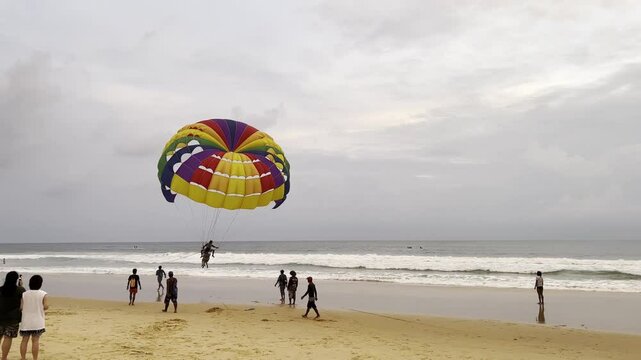 Parasailing on the beach of Phuket. Multicolored colorful parachute against the sea in cloudy weather.