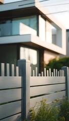 Fototapeta premium Low-angle view of a gray-toned modular fence with clean geometry, in front of a white modern cottage with wood accents and floor-to ceiling windows, pastel morning tones and soft reflections