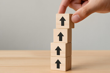 Growth and Progress: Hand placing a wooden block with an upward arrow on a growing stack of similar blocks, symbolizing upward trajectory, development, and progress.
